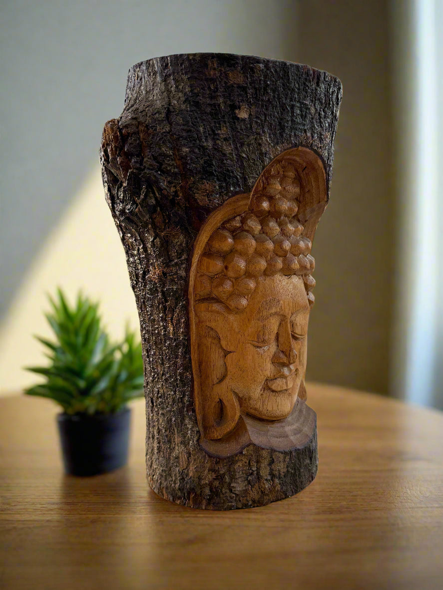 Carved Buddha head integrated into a textured tree trunk on a wooden table