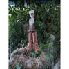 carved bird statue on wind chime with terracotta tubes hanging from a leafy tree