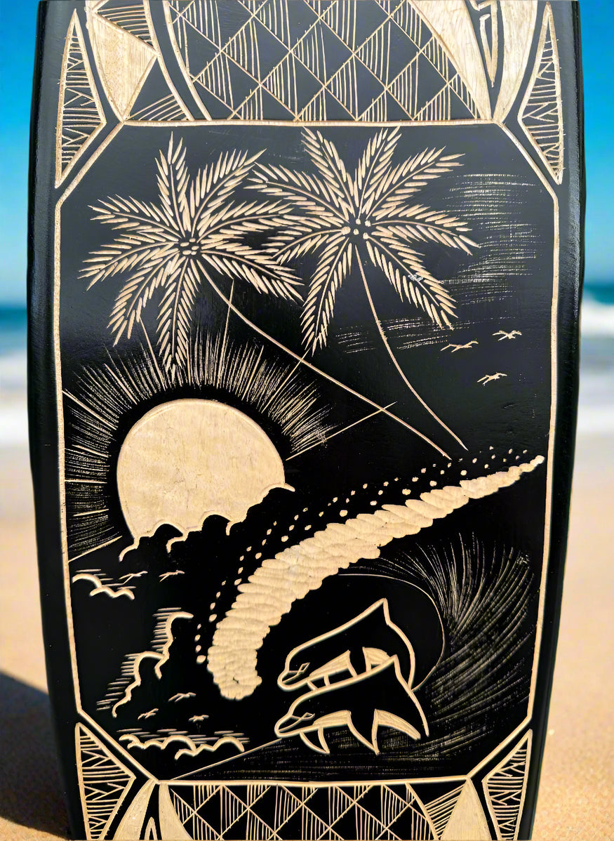Carved black panel depicting palm trees, a setting sun, waves and a sailing ship.
