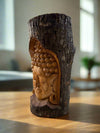Carved wooden Buddha head embedded in a tree trunk on a wooden table.