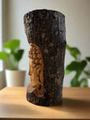 Relief carving of a Buddha head on a dark, bark-covered log