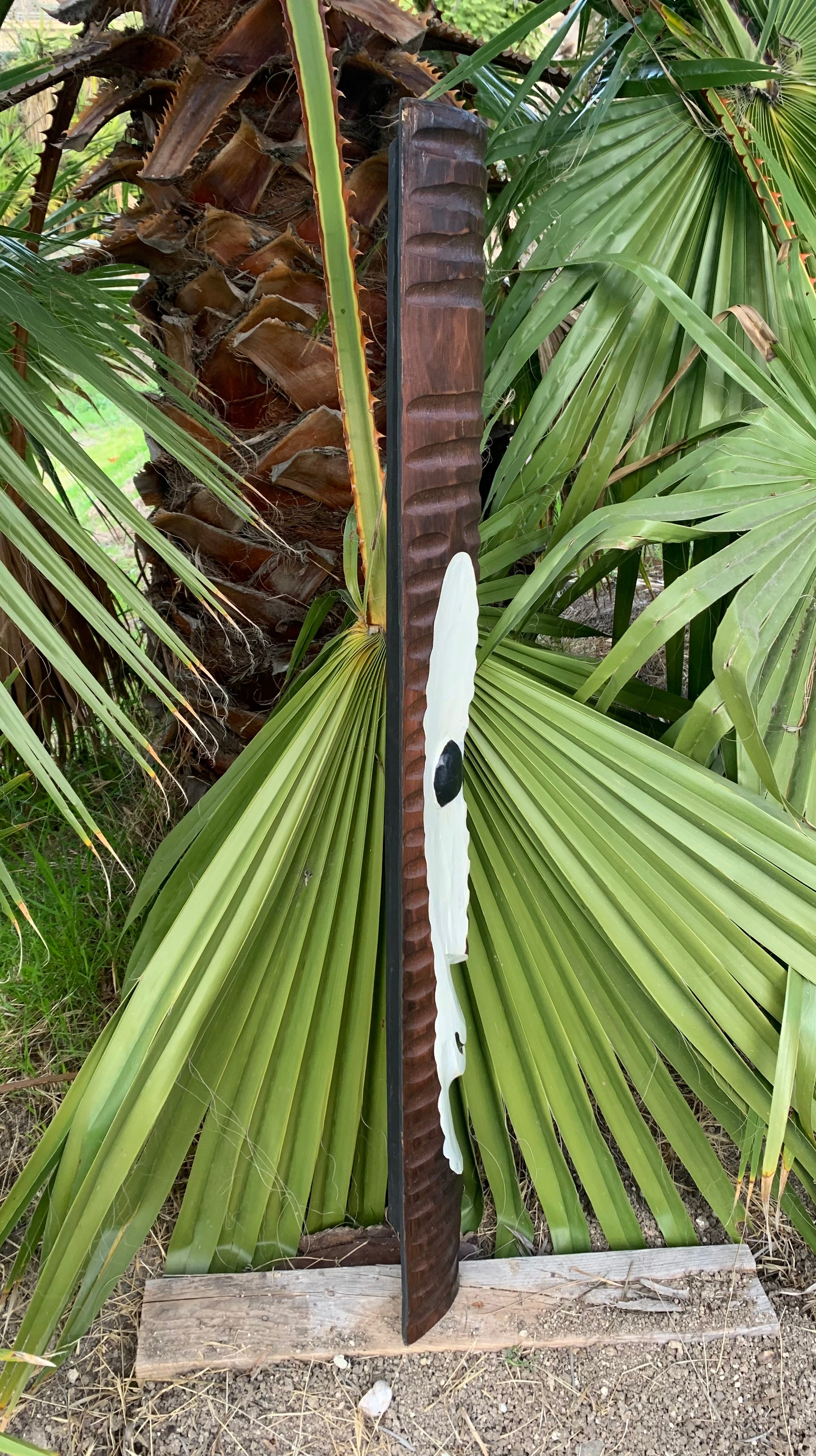 Tall ribbed wooden post beside a palm tree with large green fronds