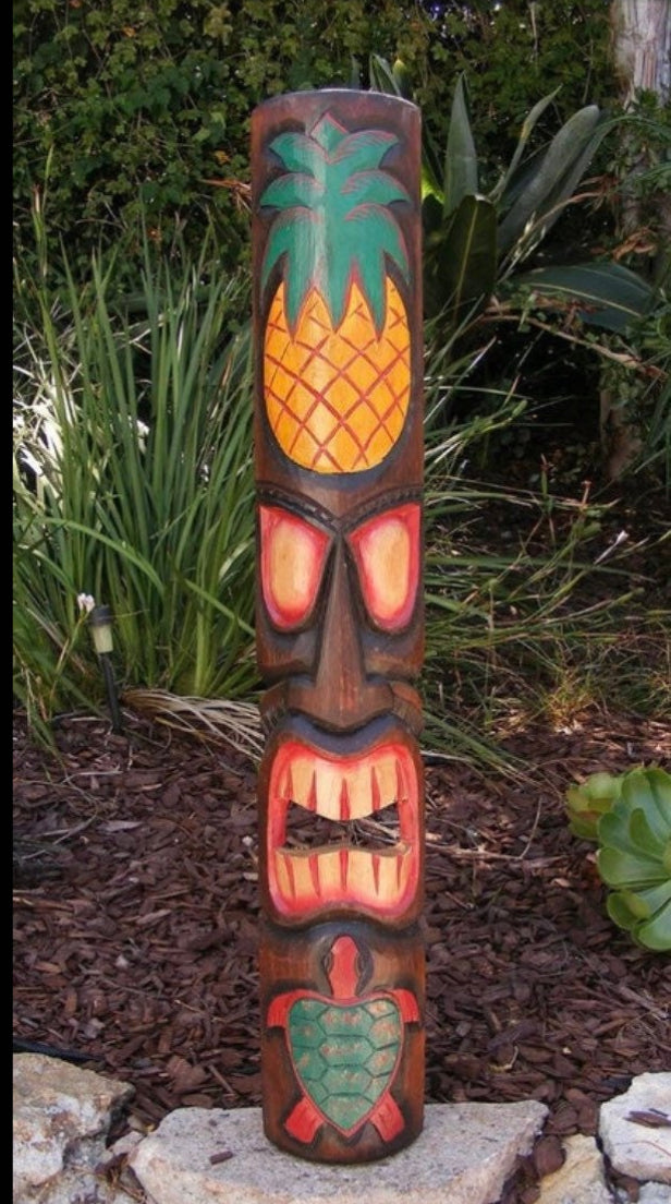 Carved wooden tiki totem featuring pineapple top and turtle at its base in a garden