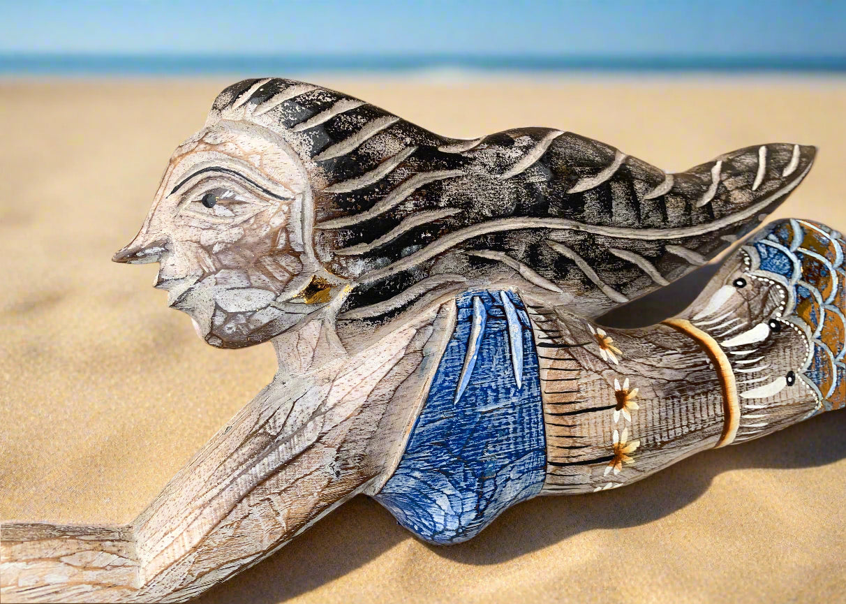Carved wooden bird sculpture on sandy beach with ocean in the background