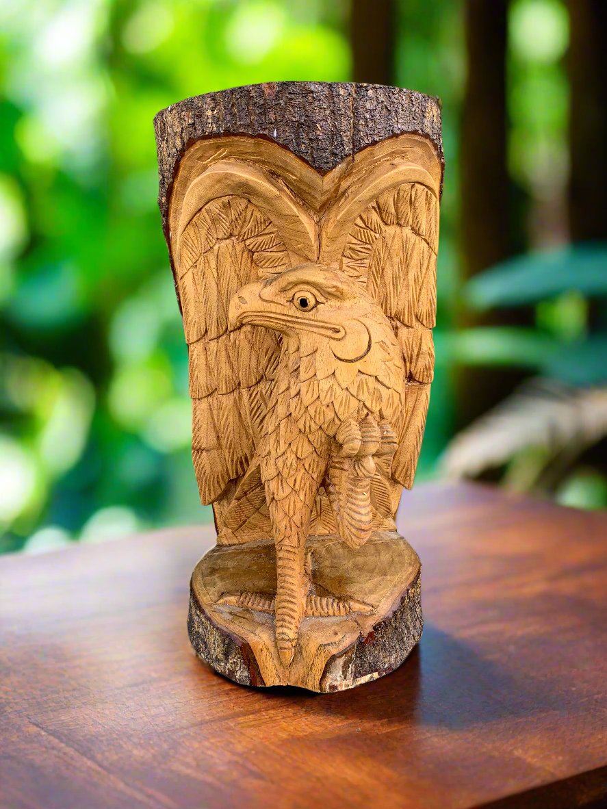 Carved wooden bird statue with outstretched wings on a stump