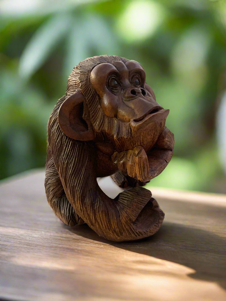 carved wooden chimpanzee figurine with hand on chin on a wooden surface