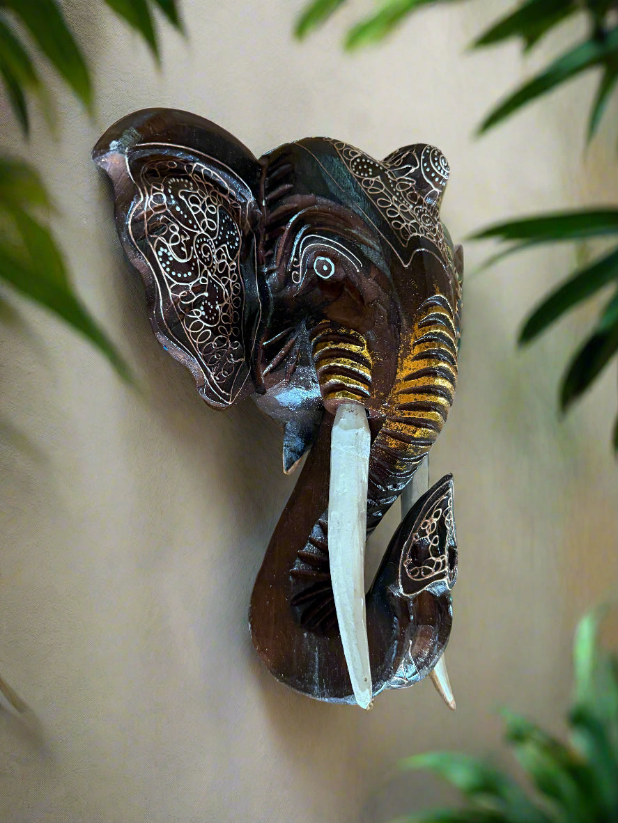 Brown wooden elephant head wall sculpture with intricate white etched patterns and long white tusks.