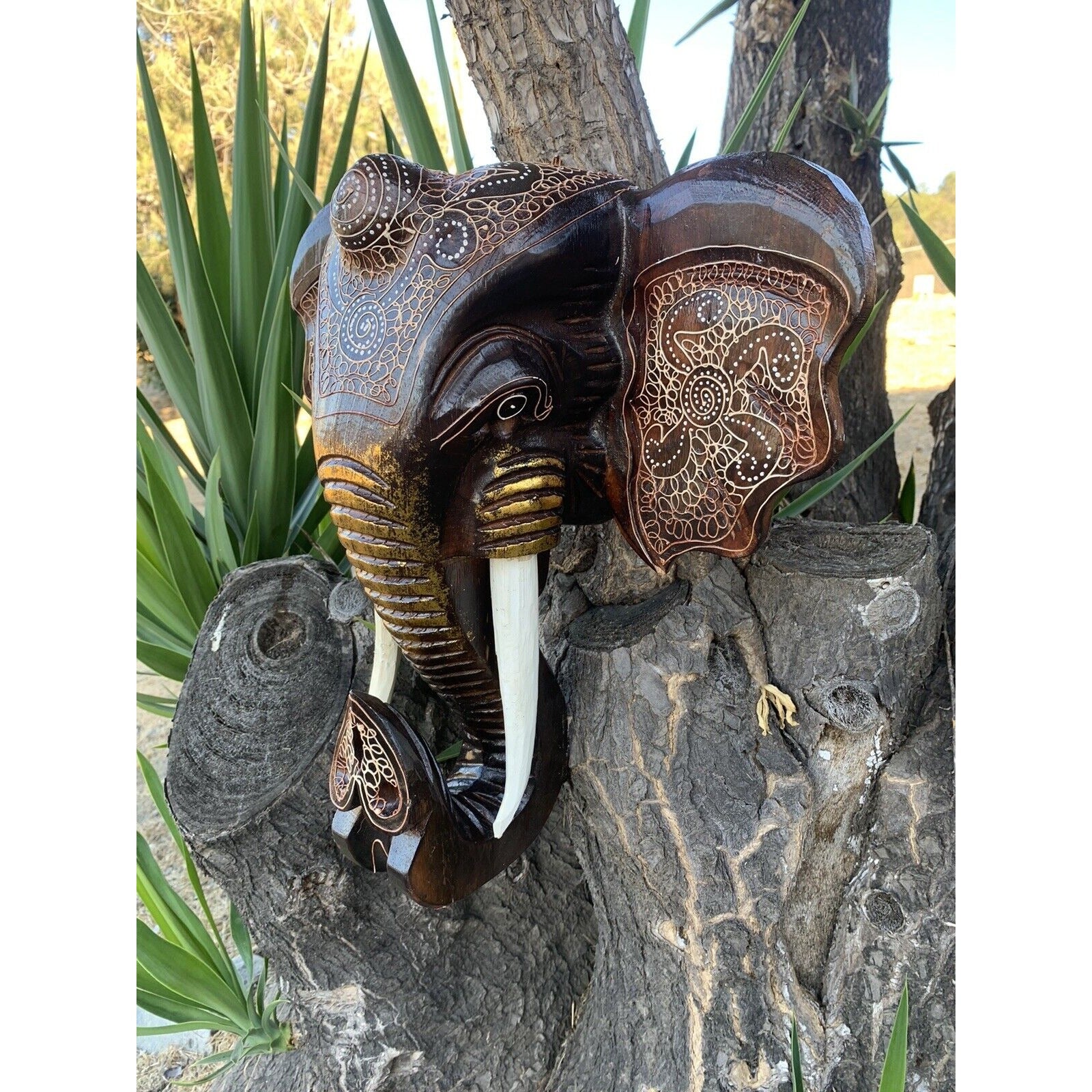 Carved wooden elephant head with intricate white patterns on a tree trunk