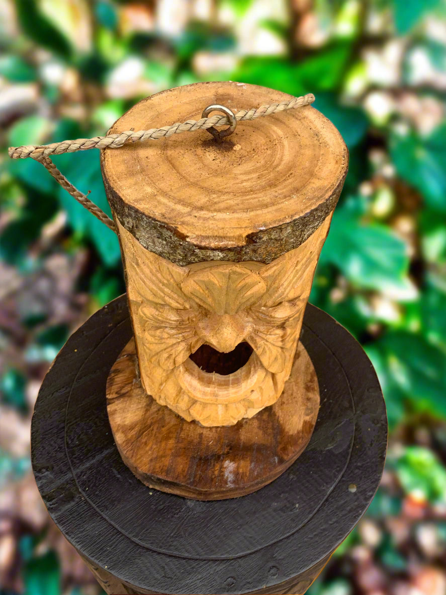 Carved wooden face totem with rope loop on top in a garden setting