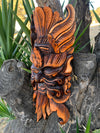 Orange and black carved wooden mask with feathered headdress mounted on a tree trunk
