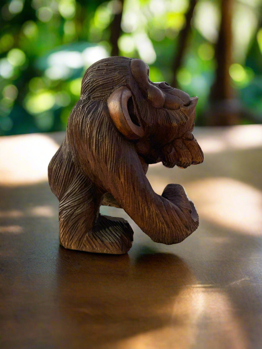 Carved wooden monkey statue on a table with a blurred garden background