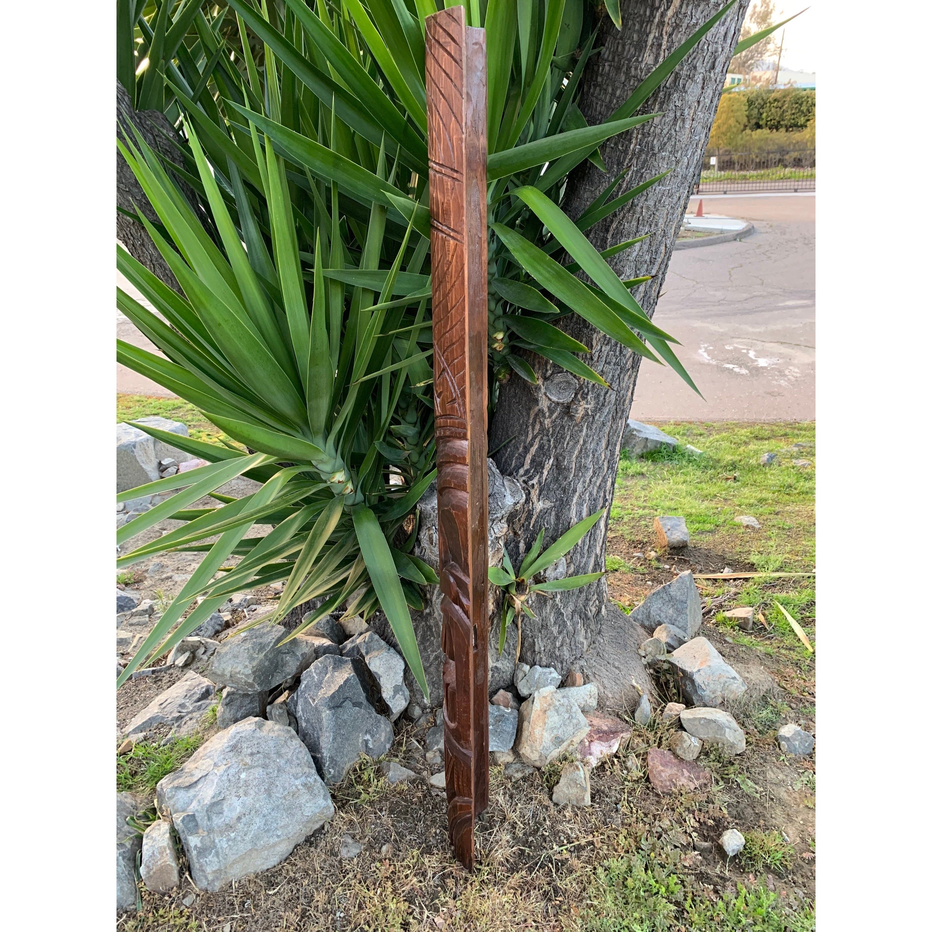 carved wooden pole leaning against a tree in a garden with rocks