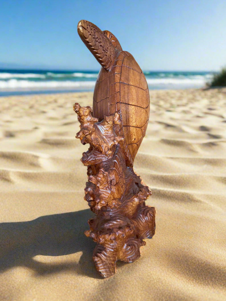 Carved wooden sea turtle sculpture on sandy beach with ocean waves in background.