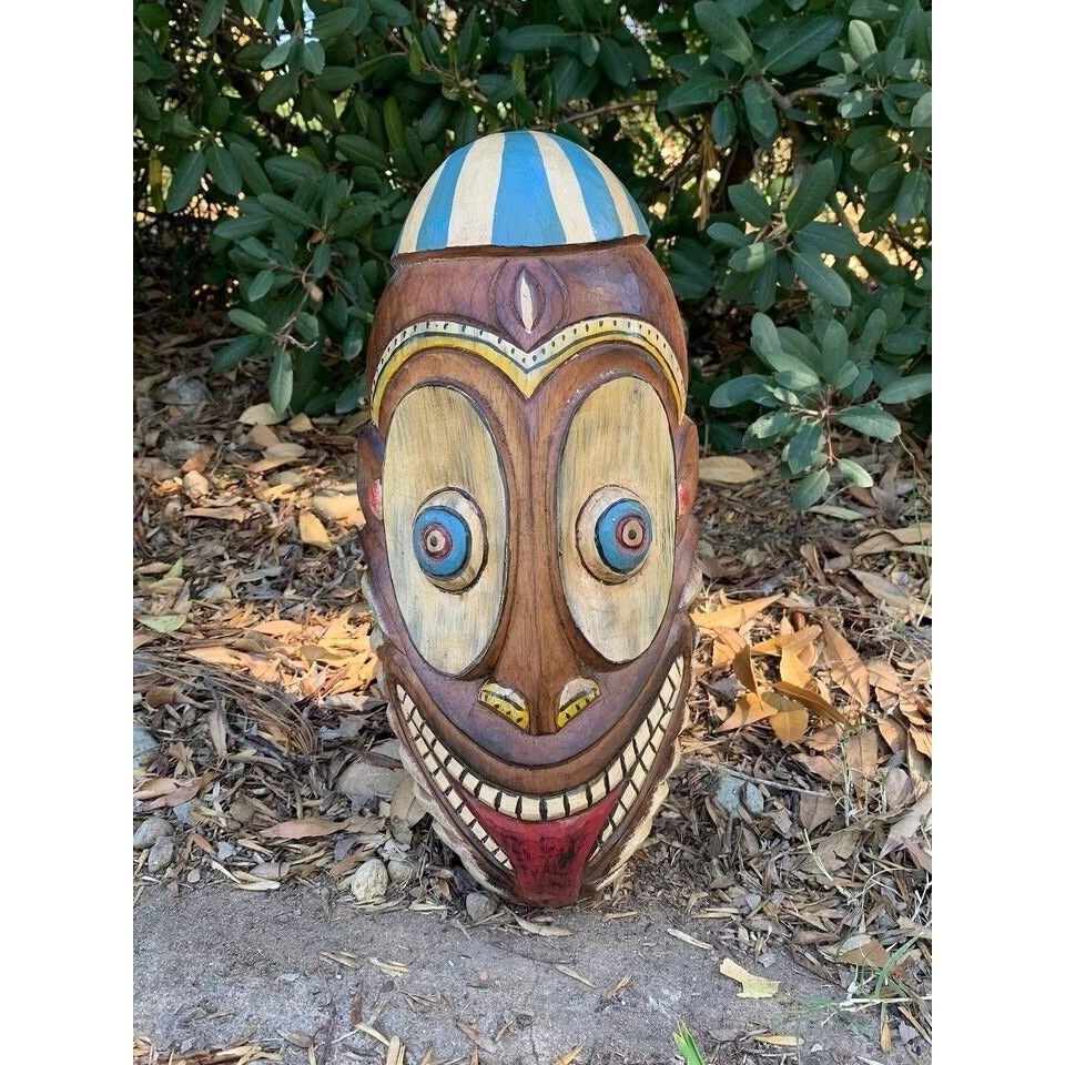 carved wooden tiki mask with oversized eyes and wide grin outdoors