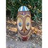 carved wooden tiki mask with oversized eyes and wide grin outdoors