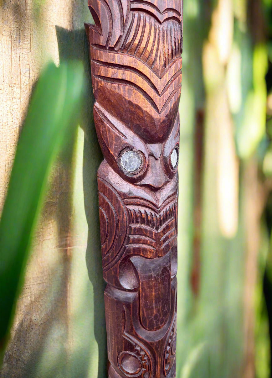 Carved wooden tiki statue with geometric patterns and large eyes on green background