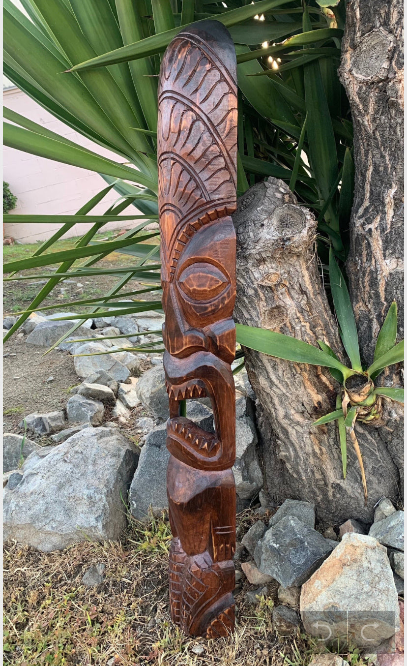 Carved wooden tiki statue with open mouth in garden setting