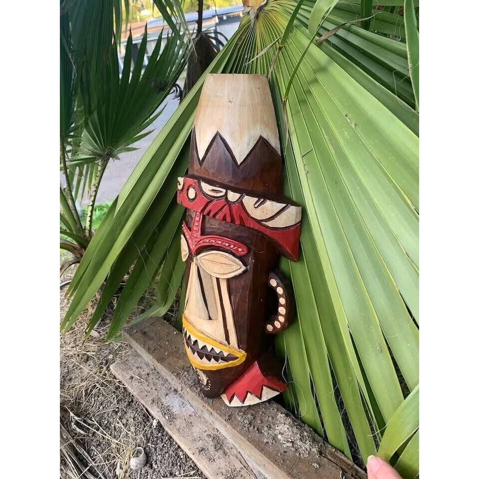 Carved wooden tiki statue among broad palm leaves in a garden