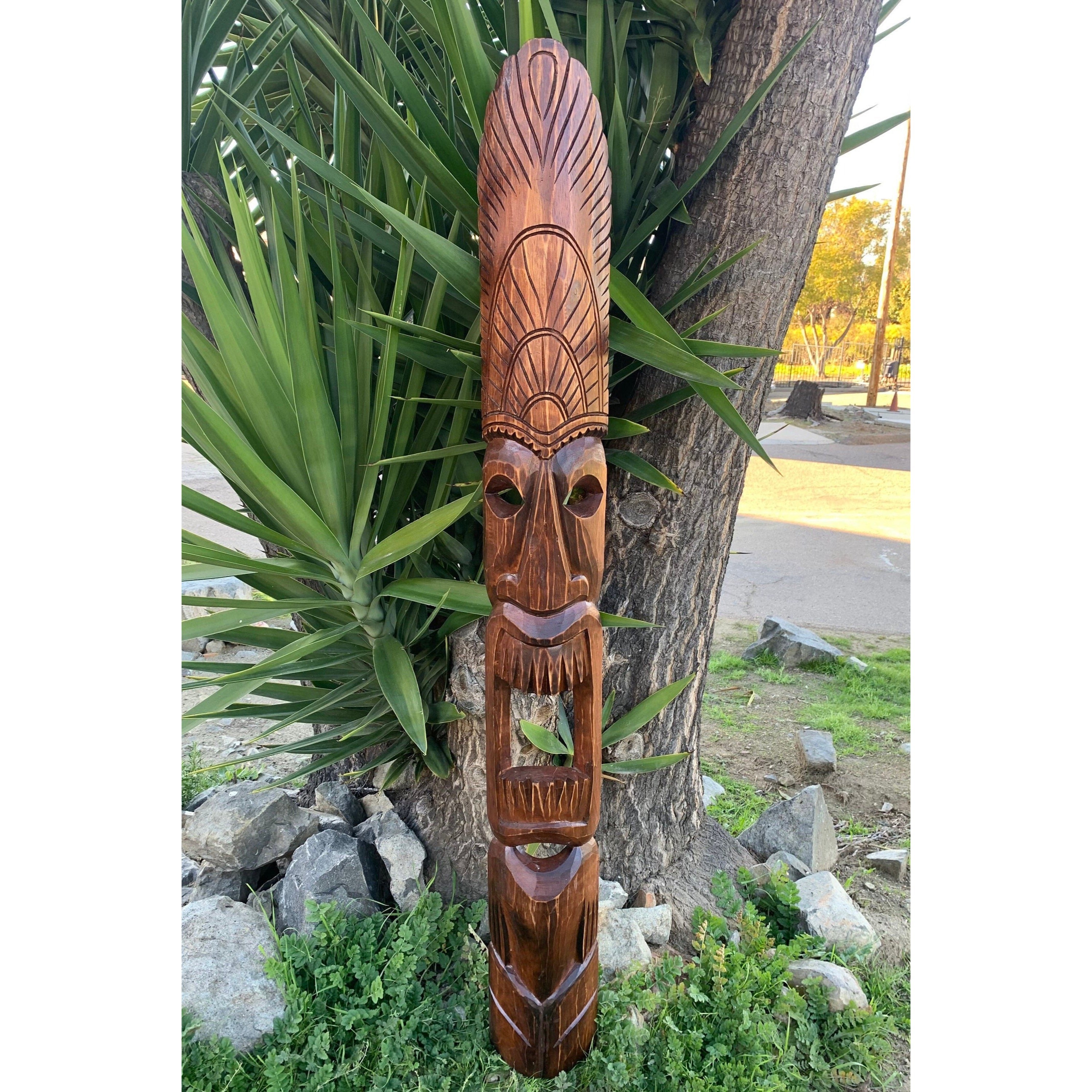 Carved wooden tiki statue leaning against a tree in a garden.