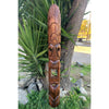 Carved wooden tiki statue leaning against a tree in a garden.