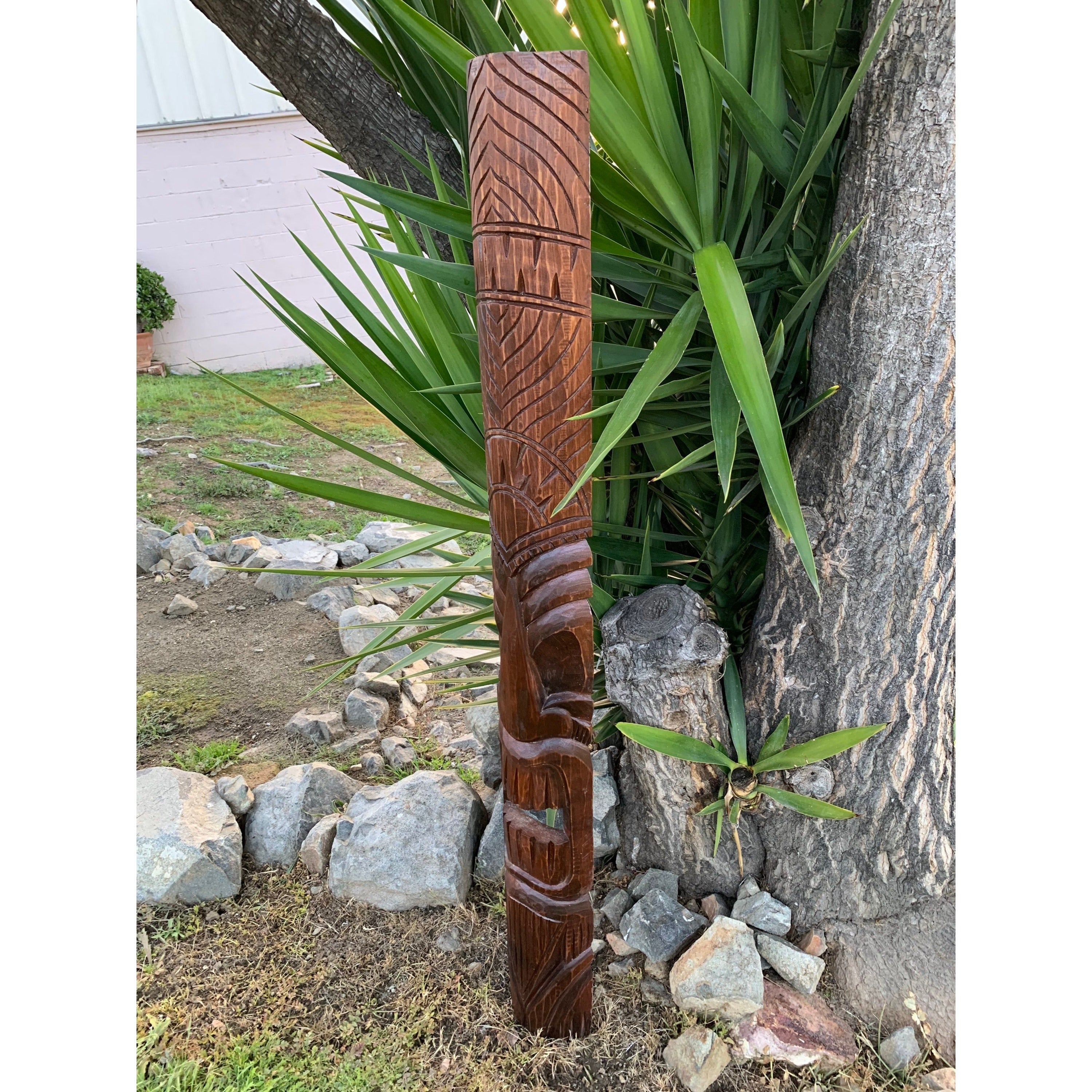 Carved wooden tiki totem pole beside a tree in a garden with rocks