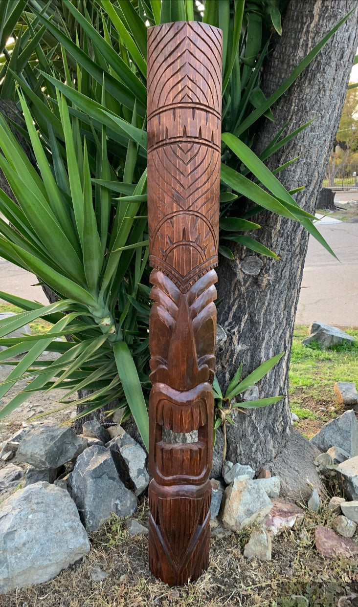 Carved wooden tiki totem pole with geometric patterns and a carved face outdoors.
