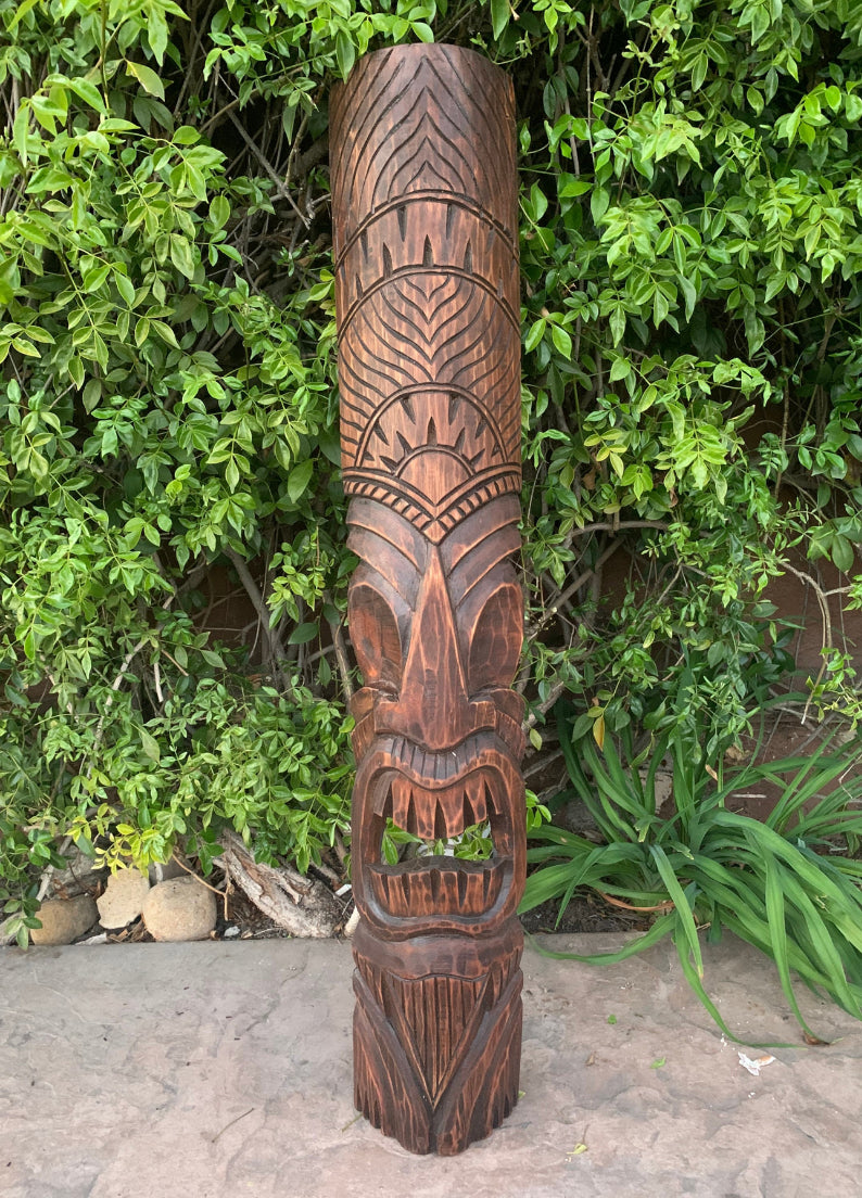Carved wooden tiki totem pole with geometric patterns in a garden