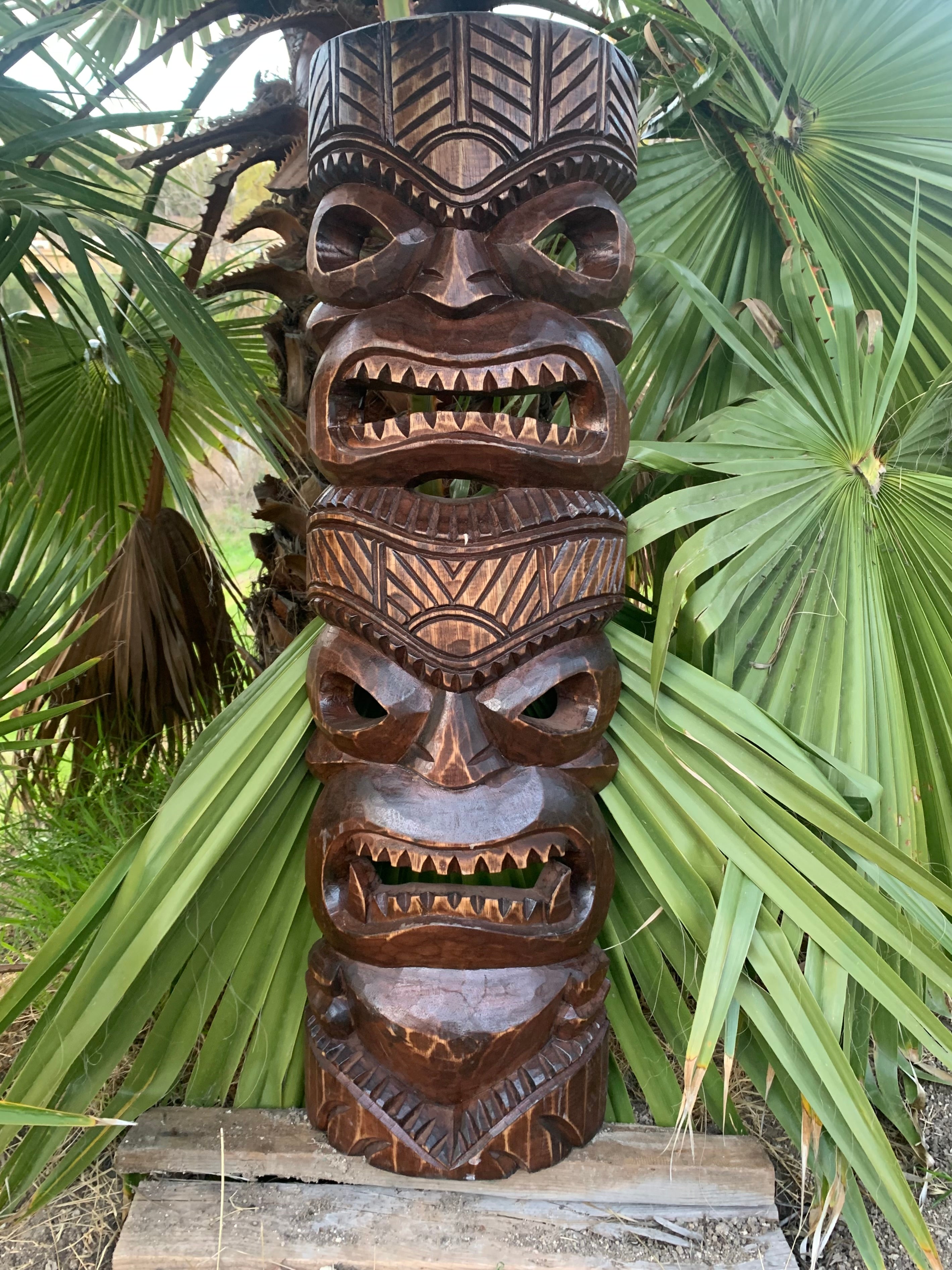 carved wooden tiki totem pole with multiple faces in a palm garden