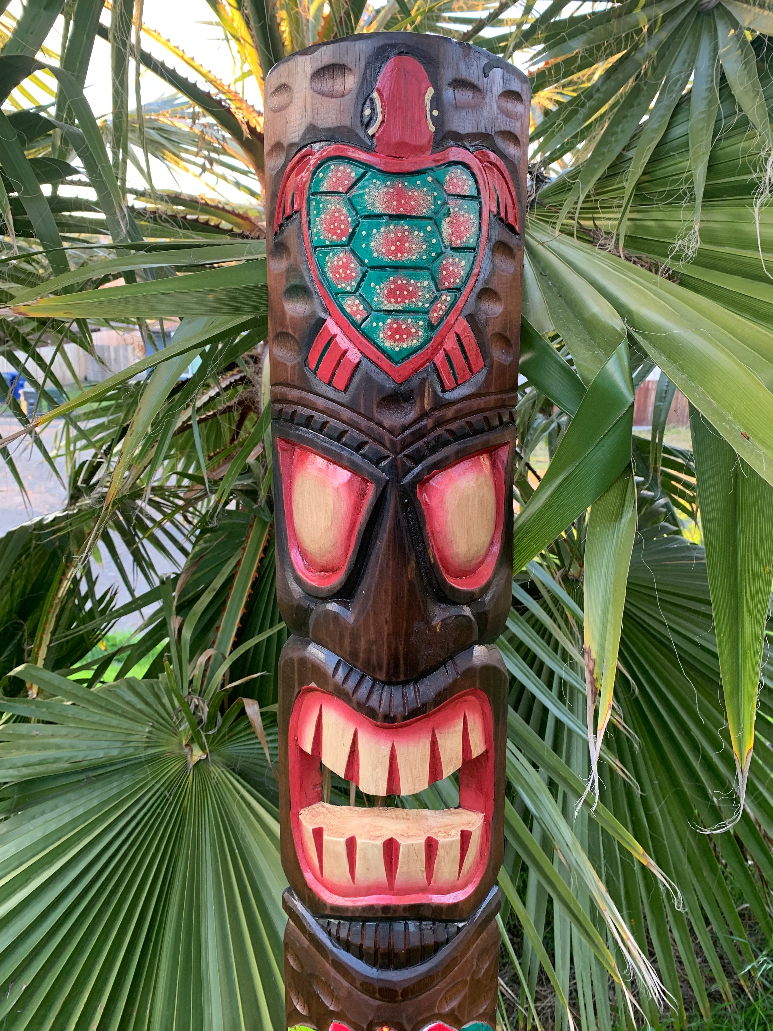 Carved wooden tiki totem pole with turquoise turtle motif on top, among palm leaves