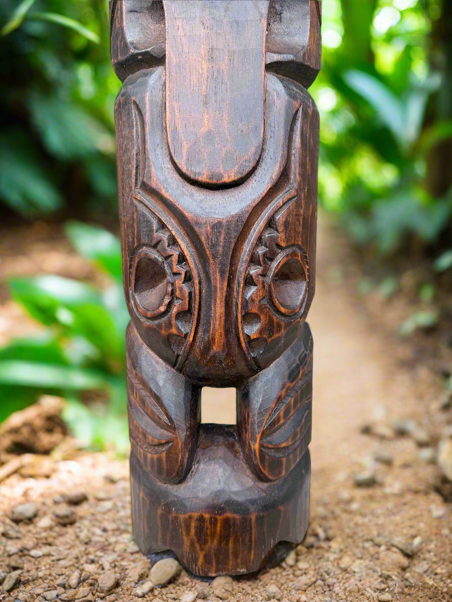 Close-up of a dark carved wooden totem with circular gear-like patterns in a garden path