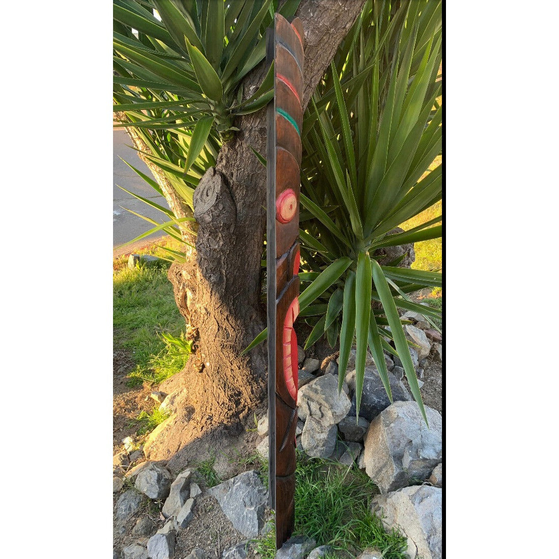 Carved wooden totem pole beside a tree in a rocky garden