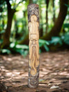 Carved wooden totem pole with bearded face in a forest setting