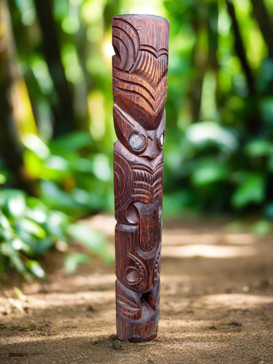 Carved wooden totem pole standing upright on a dirt path in a lush green forest.
