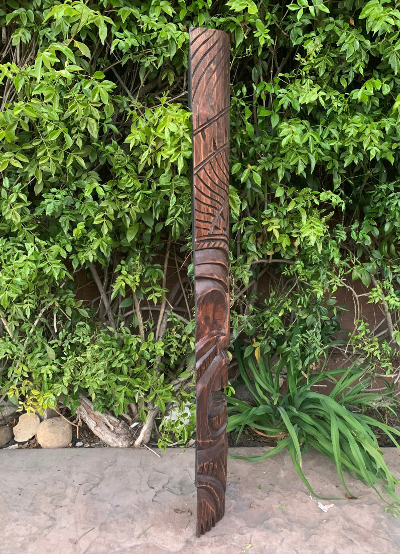 Carved wooden totem pole standing in a garden with lush green foliage