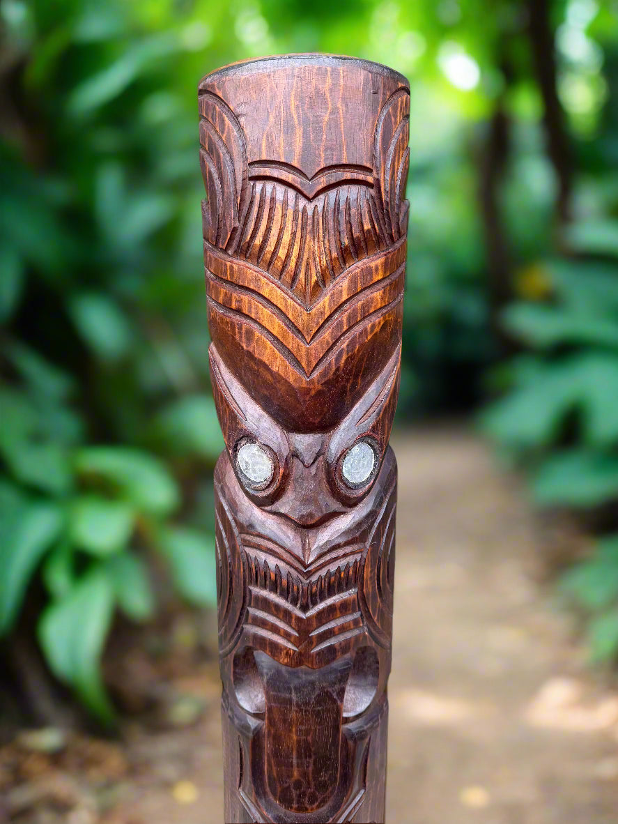Carved wooden totem pole with owl-like face in a lush garden setting