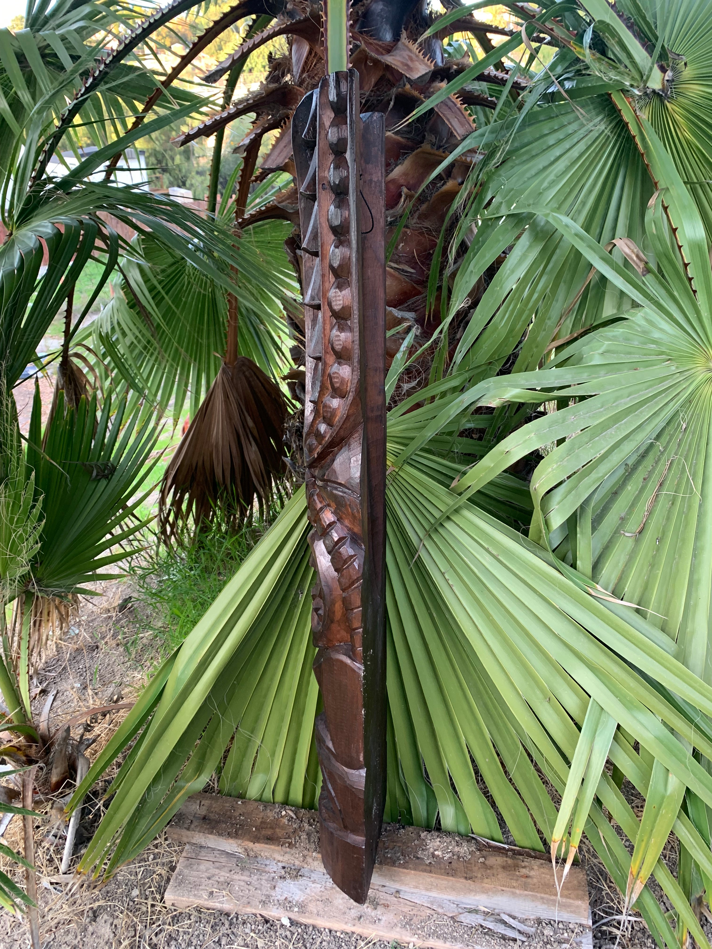 Carved wooden totem-staff with knobbed design among palm fronds in a garden.