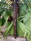 Carved wooden totem-staff with knobbed design among palm fronds in a garden.