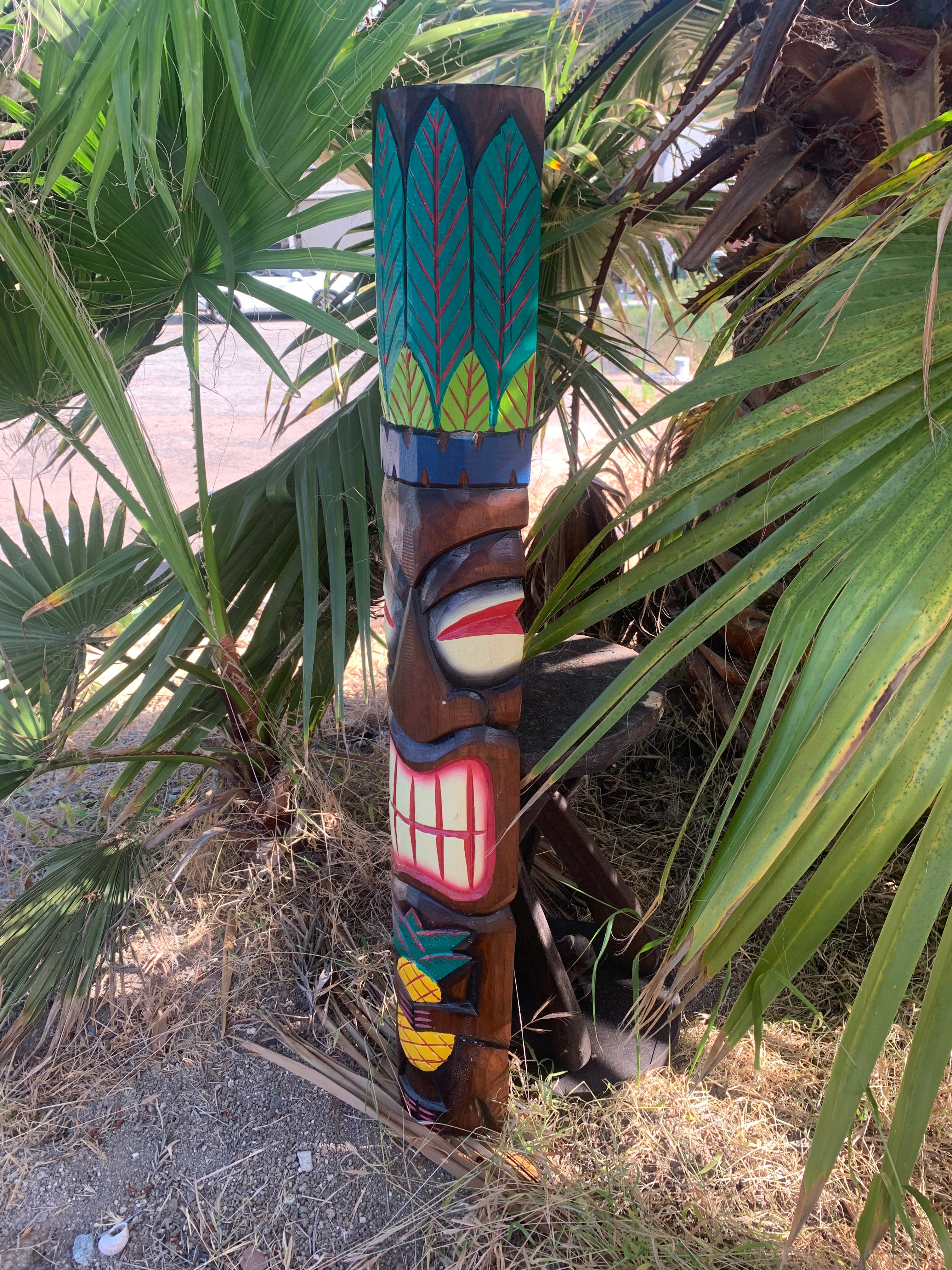 Colorful carved tiki totem pole with geometric leaf patterns among palm fronds
