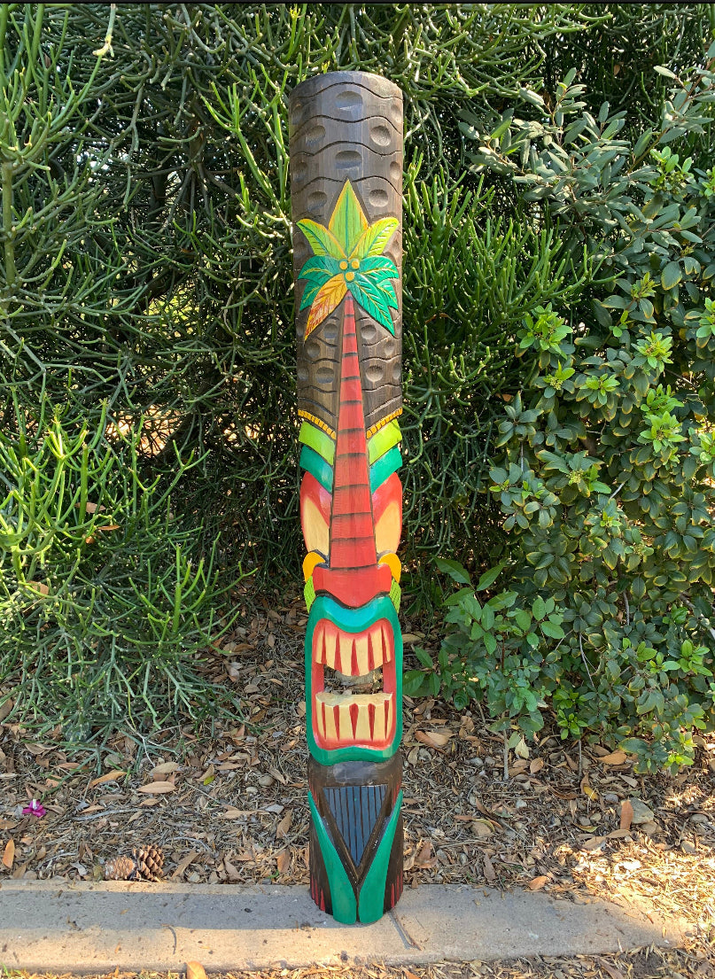 Colorful carved tiki totem pole in a garden surrounded by green shrubs.