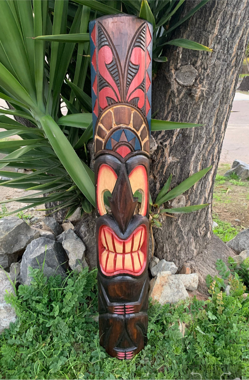 Colorful carved tiki totem pole attached to a tree trunk in a garden.