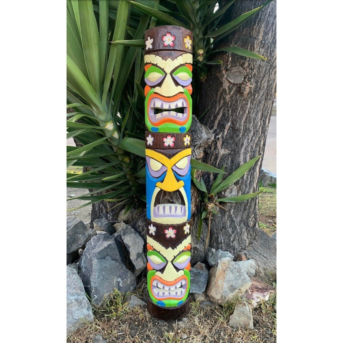 Colorful carved tiki totem pole with multiple faces outdoors beside a tree