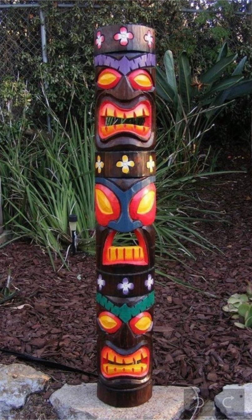Colorful carved tiki totem pole with multiple faces in a garden.
