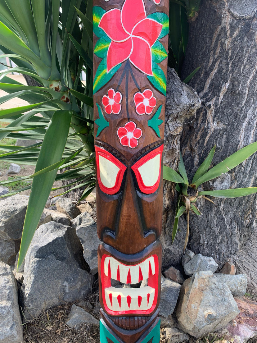 Colorful carved wooden totem pole featuring red-eyed face, white teeth, and flower motifs