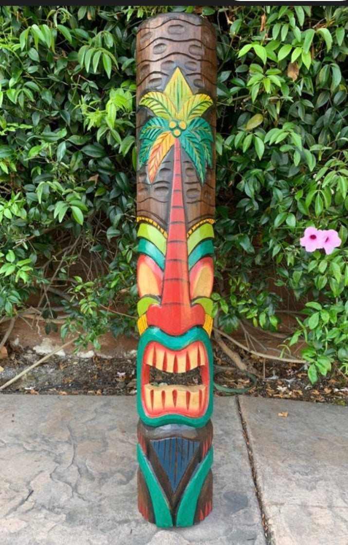 Colorful carved wooden totem pole with palm tree design outdoors among greenery