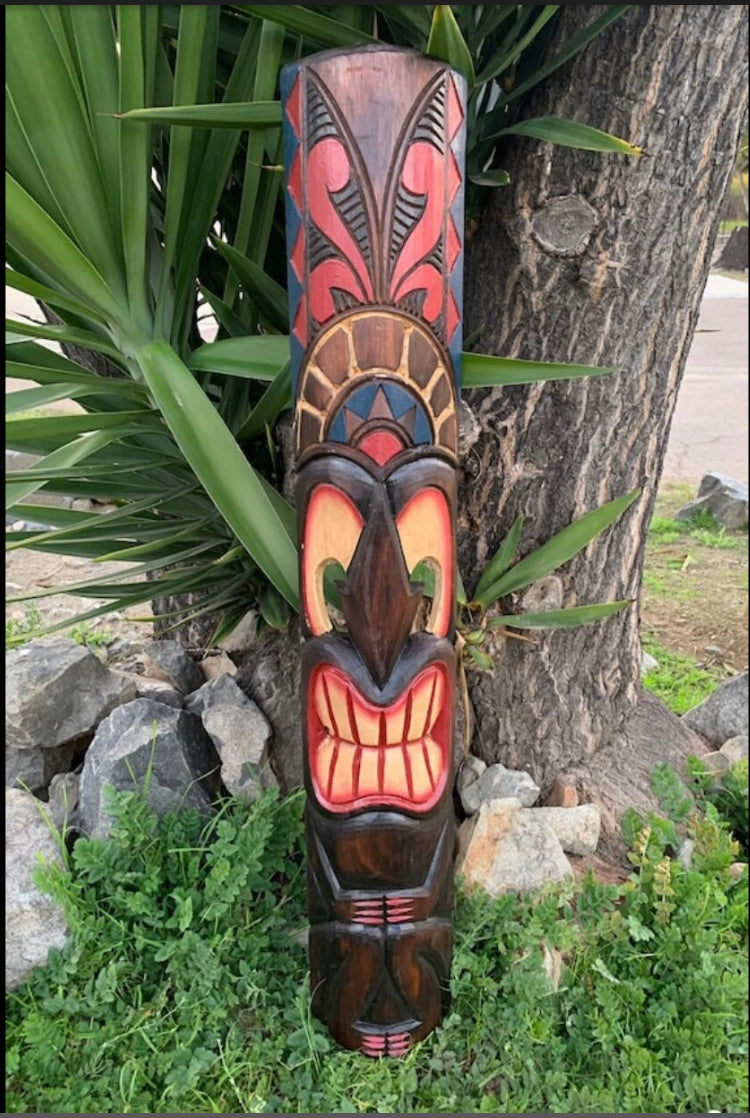 Colorful carved wooden totem pole with geometric patterns beside a tree outdoors