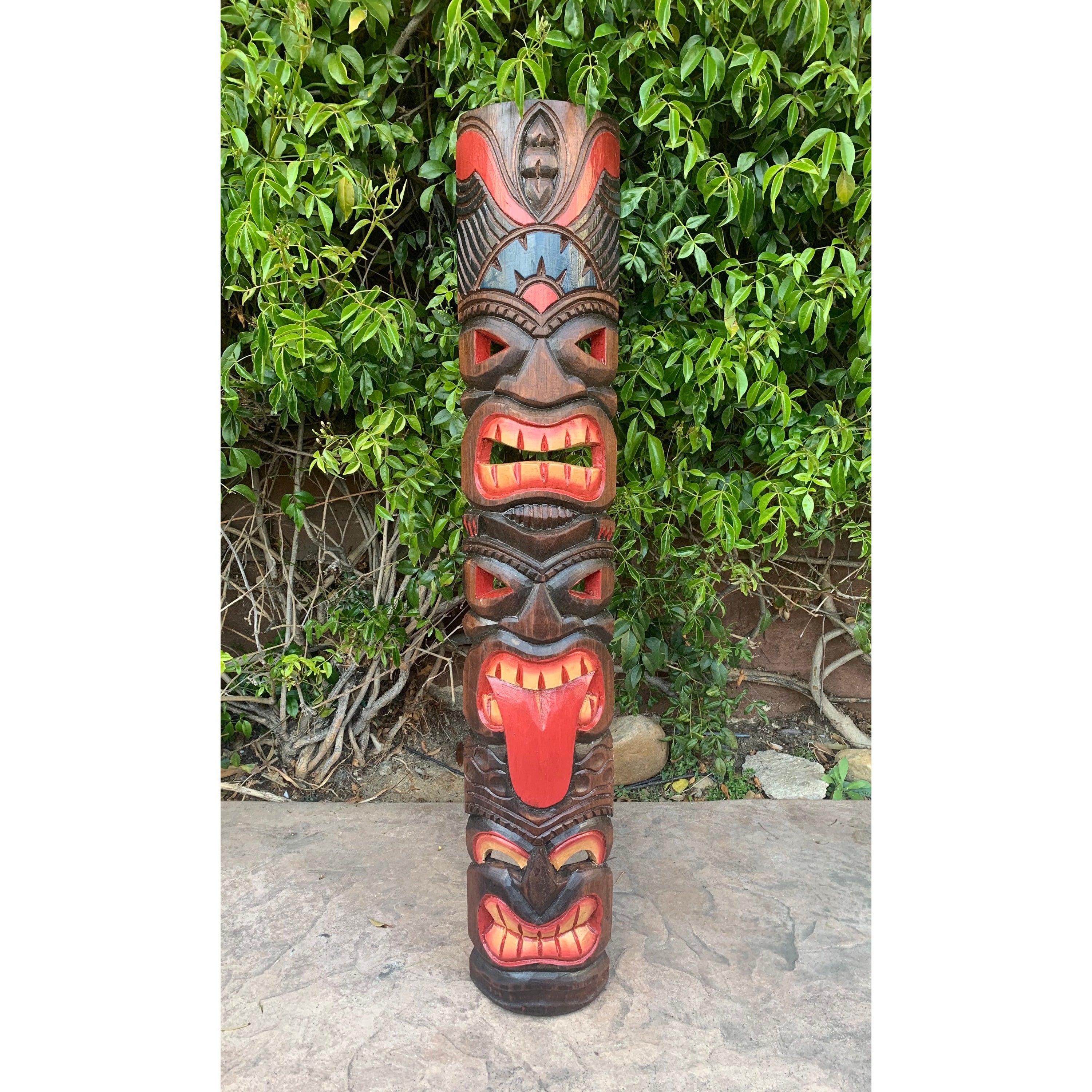 Colorful carved wooden totem pole with multiple faces and red tongues against green foliage.