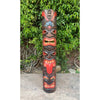 Colorful carved wooden totem pole with multiple faces and red tongues against green foliage.