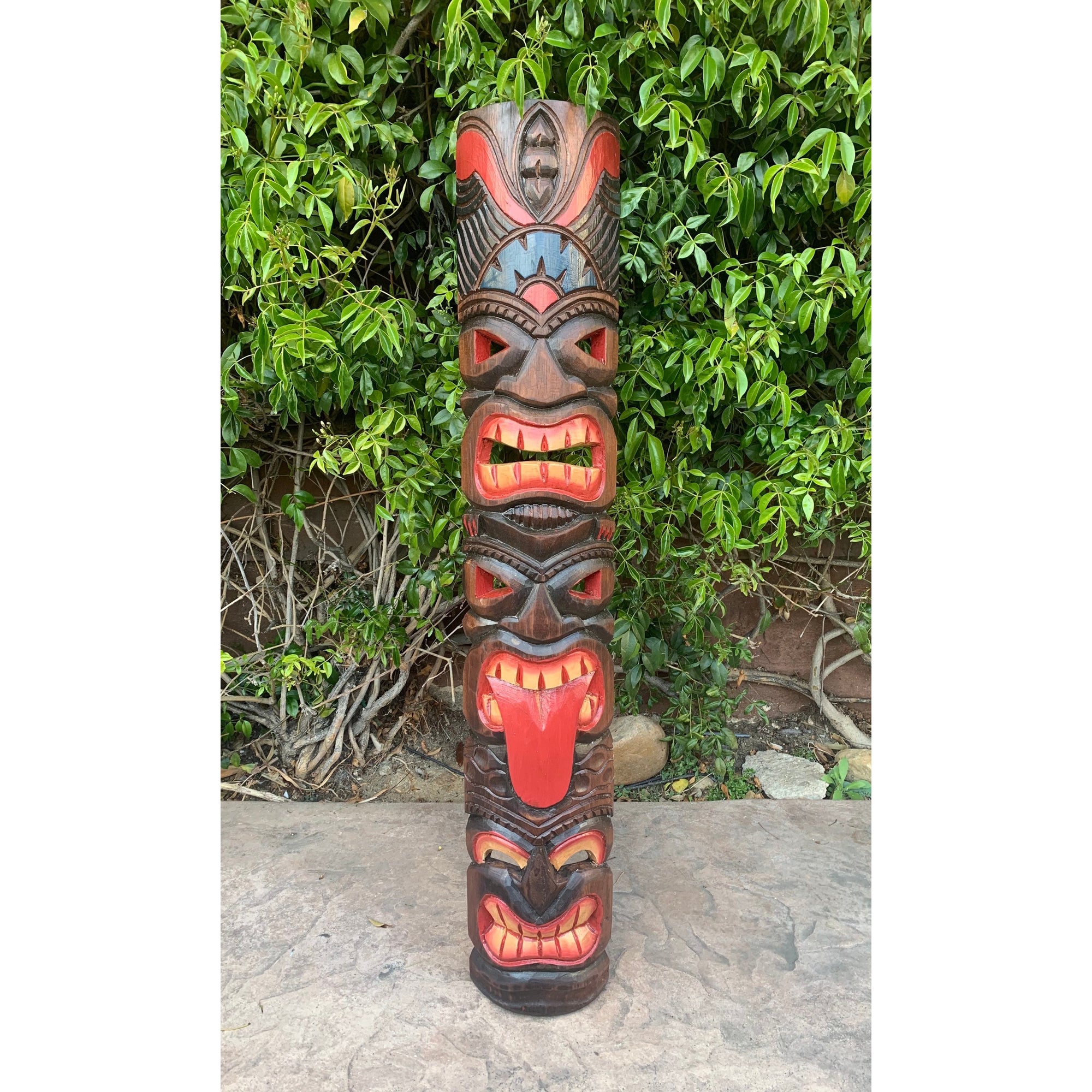 Colorful carved wooden totem pole with multiple faces and red tongues against green foliage.