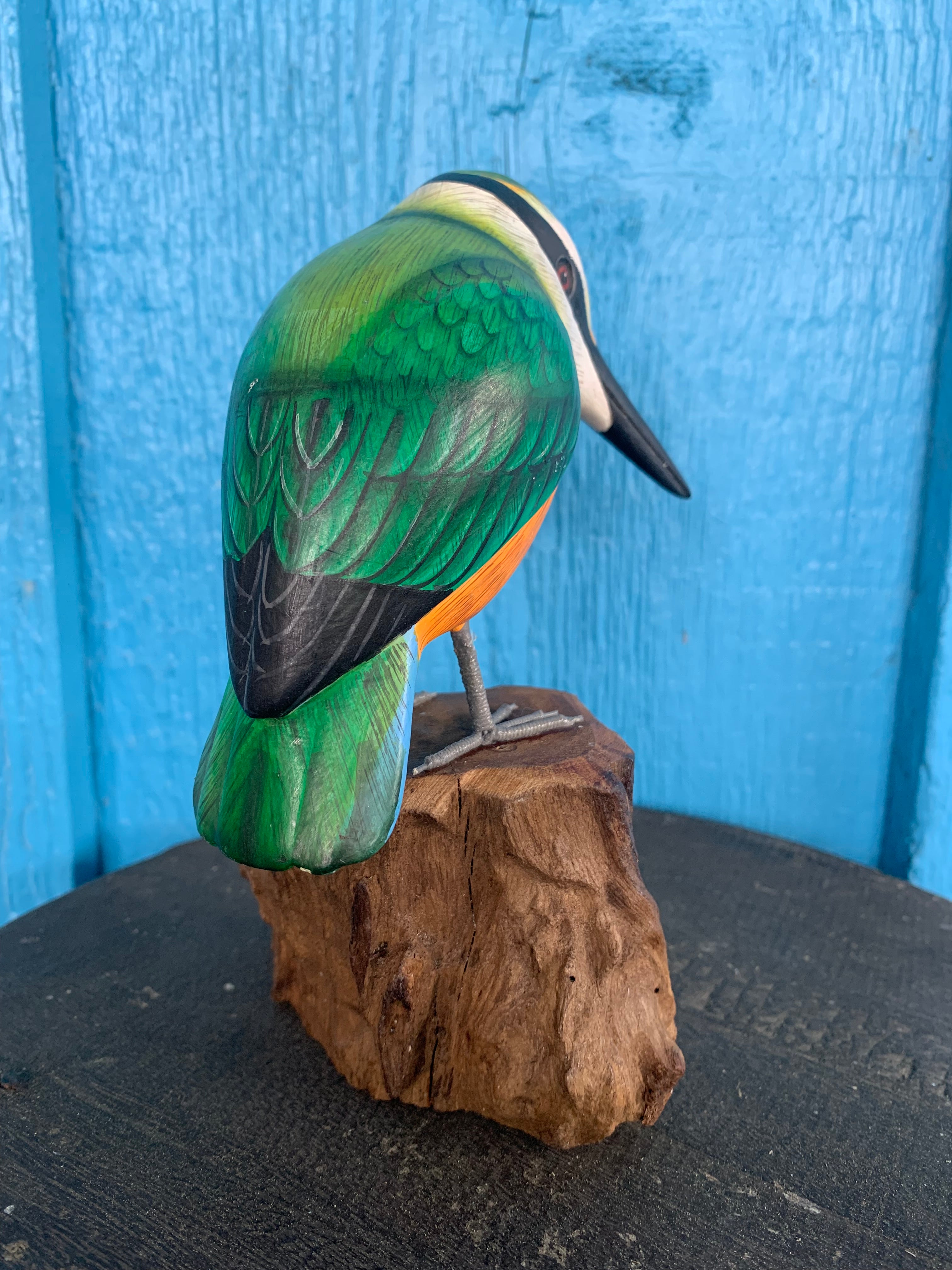 Colorful green hummingbird wooden sculpture perched on a rock against a blue background.