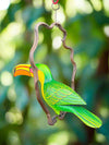 Colorful green parrot ornament hanging on a curved metal frame with a blurred green background